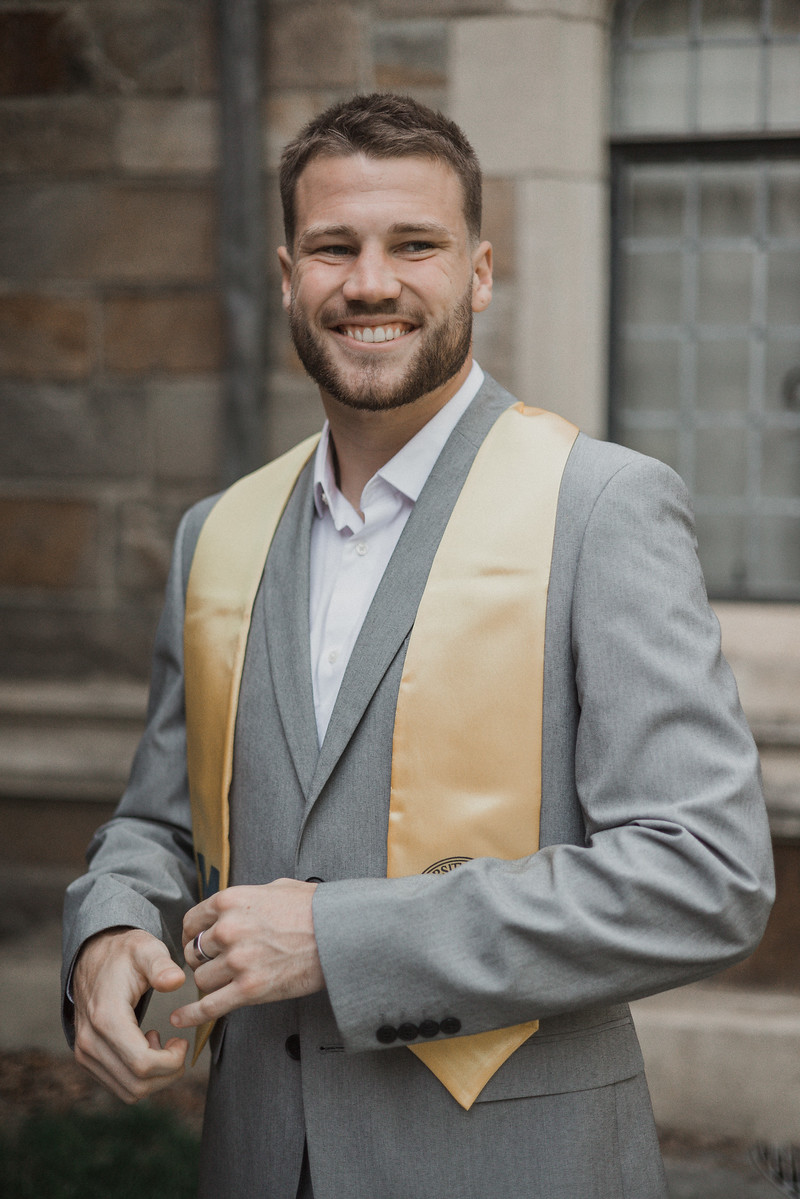 A graduate in a gray suit smiling at the camera